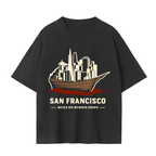 A black short-sleeve t-shirt with a graphic print of a wooden ship buried beneath SF skyline, with the text 'SAN FRANCISCO BUILT ON BURIED SHIPS' underneath.