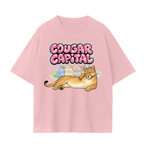 A light pink faded short-sleeve t-shirt featuring a graphic print of a cougar lying down in front of painted lady houses.
