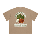 A faded tan short-sleeve t-shirt shown from the back, featuring a large graphic print of a red apple with leaves and text that reads 'FARMERS MARKET RICH', 'seasonal only - peak ripeness', and 'FOG & FORM FARMS'.