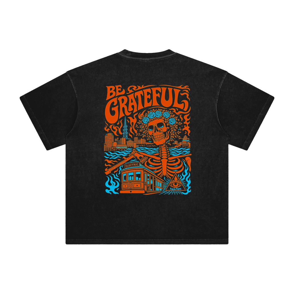 A black short-sleeve t-shirt with a large colorful graphic on the back. The graphic features the words 'BE GRATEFUL' in orange, a skull with a floral crown, a skeleton, a house, and blue waves for SF music.