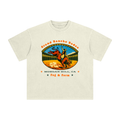 An off-white short-sleeve t-shirt with a vintage-style graphic of a cowboy riding a bucking bull in a rodeo arena in South Bay.