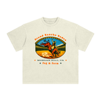 An off-white short-sleeve t-shirt with a vintage-style graphic of a cowboy riding a bucking bull in a rodeo arena in South Bay.